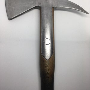 Puede incluir: Un hacha de plata con mango de madera. La cabeza del hacha tiene una hoja curva y un peque&ntilde;o dise&ntilde;o circular en el mango.