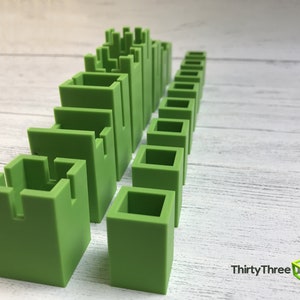 May include: A set of green plastic building blocks of varying sizes and shapes. The blocks are arranged in a row, with the tallest blocks at the left and the shortest blocks at the right. The blocks are all the same color, and they have a smooth, matte finish.