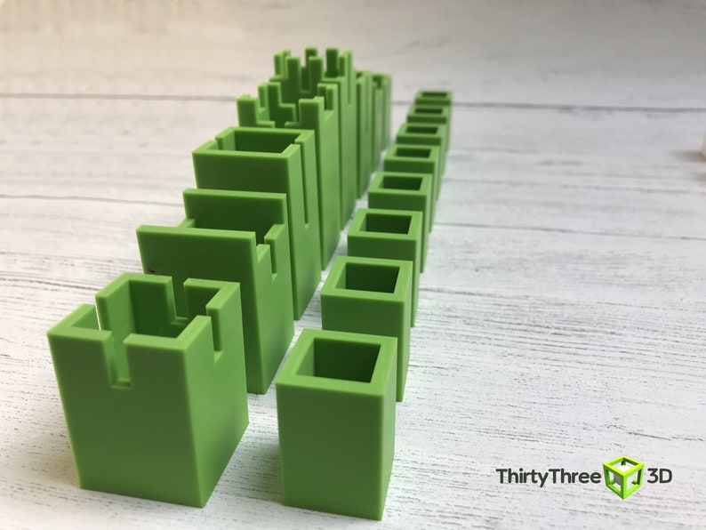 May include: A set of green plastic building blocks of varying sizes and shapes. The blocks are arranged in a row, with the tallest blocks at the left and the shortest blocks at the right. The blocks are all the same color, and they have a smooth, matte finish.