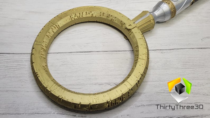 May include: A gold-colored ring with intricate details and a silver handle. The ring is circular and has a textured surface.