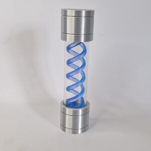 May include: A cylindrical container with a clear tube and metallic silver caps at the top and bottom. Inside the tube is a blue, double-helix shaped structure. The container is standing upright against a white background.