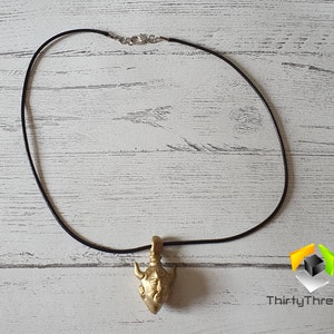 May include: A gold-colored pendant necklace with a detailed bull head design. The necklace is on a black cord.