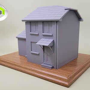 May include: A gray 3D printed model of a two-story house with a brown wooden base. The house has a gray roof, windows, and a door.