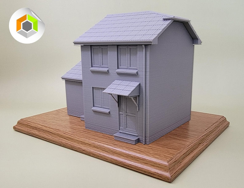 May include: A gray 3D printed model of a two-story house with a brown wooden base. The house has a gray roof, windows, and a door.