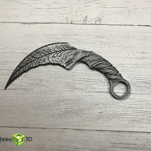 May include: A silver-colored metal throwing knife with a curved blade and a ring at the end of the handle.