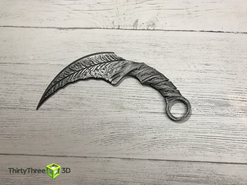 May include: A silver-colored metal throwing knife with a curved blade and a ring at the end of the handle.