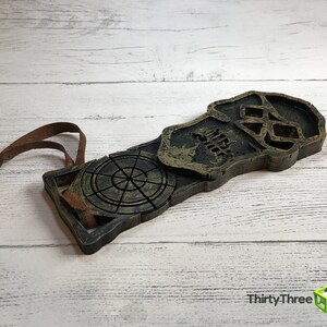 May include: A wooden skull and compass ornament with a brown leather cord attached. The skull is carved with a detailed design and the compass has a circular face with a compass rose.