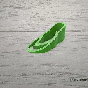 May include: A green plastic doorstop shaped like a shoe. The doorstop is on a light wood surface.