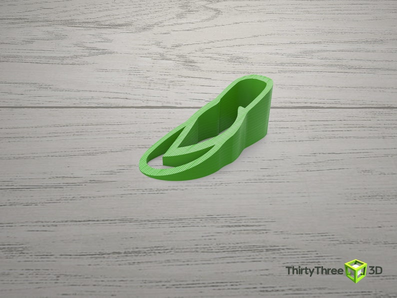 May include: A green plastic doorstop shaped like a shoe. The doorstop is on a light wood surface.