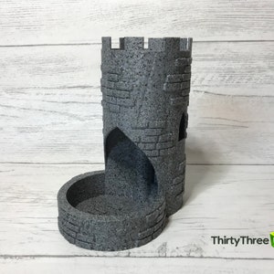 May include: A gray stone tower-shaped dice tower with a rounded base and a small opening on the side. The tower has a textured surface that resembles stone.