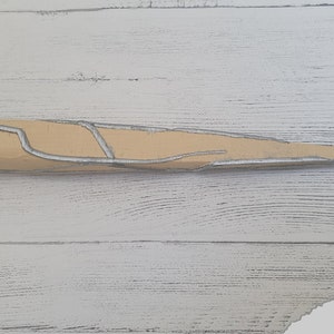Op de afbeelding: Een beige en zilverkleurig dolk met een getextureerd oppervlak. De dolk heeft een puntige punt en een afgeronde handgreep.