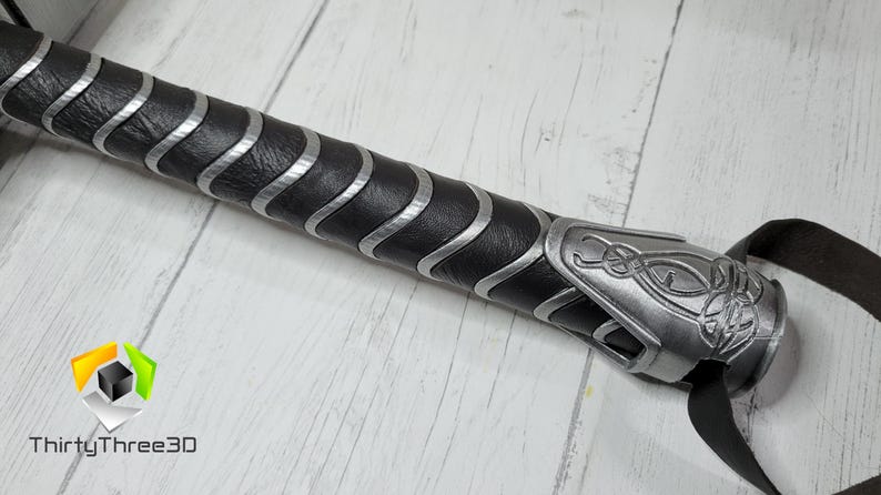 May include: Close-up of a black and silver handle with a leather grip and a silver metal cap with a decorative design. The handle is for a prop weapon.