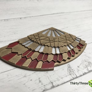 K&ouml;nnte beinhalten: Ein 3D-gedrucktes Dekorationsst&uuml;ck in Gold und Rot mit geometrischem Design. Das St&uuml;ck ist in Form eines F&auml;chers oder eines Fl&uuml;gels.