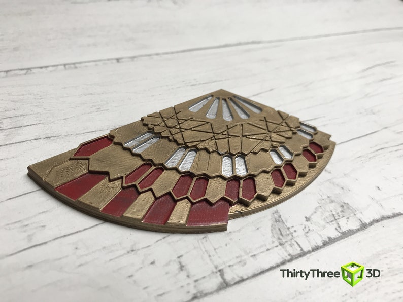 K&ouml;nnte beinhalten: Ein 3D-gedrucktes Dekorationsst&uuml;ck in Gold und Rot mit geometrischem Design. Das St&uuml;ck ist in Form eines F&auml;chers oder eines Fl&uuml;gels.