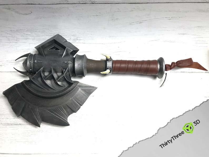 May include: A silver axe with a brown leather handle and a silver skull-like design on the head. The axe has a decorative knot at the end of the handle.