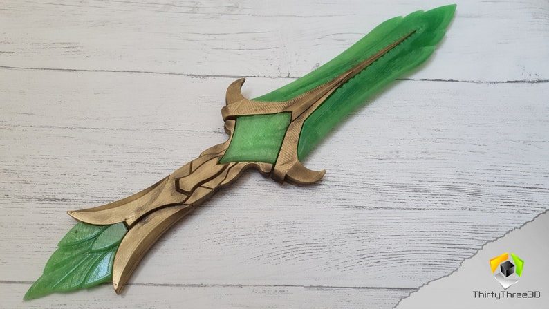 May include: A green and gold decorative sword with a detailed design. The blade is green and the hilt is gold with intricate details.