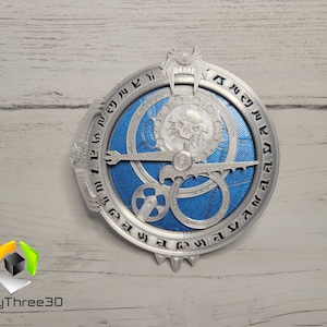 Puede incluir: Una br&uacute;jula de metal de color plateado con un centro azul y un dise&ntilde;o de engranaje. La br&uacute;jula tiene una forma circular y est&aacute; rodeada por un anillo de n&uacute;meros.