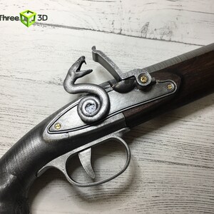 Puede incluir: Primer plano de una r&eacute;plica de pistola de chispa. La pistola presenta un acabado met&aacute;lico plateado con un dise&ntilde;o de serpiente decorativa en la cerradura. La culata de madera es de color marr&oacute;n oscuro, y el gatillo y el martillo son visibles.