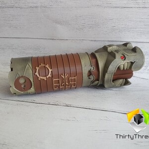 May include: A 3D printed, brown and grey, steampunk-style, dragon head pipe. The dragon has a red eye and sharp teeth. The pipe is decorated with gears and other intricate details.