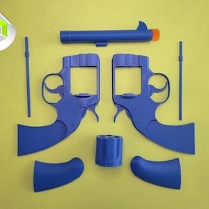 Op de afbeelding: Een gedemonteerde speelgoedpistoolset van blauw plastic, met twee pistoolframes, een loop met een oranje punt, een cilinder, twee handgrepen en twee staven. De onderdelen zijn gerangschikt op een gele achtergrond.