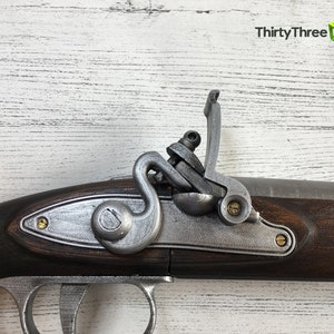 Puede incluir: Primer plano de una r&eacute;plica de pistola de chispa. La pistola presenta una culata de madera marr&oacute;n oscuro, componentes met&aacute;licos plateados y detalles de lat&oacute;n. La imagen incluye el texto "ThirtyThree 3D".