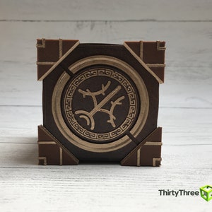 May include: A brown wooden box with a gold-colored circular design on the front. The design features a stylized tree with branches and leaves.