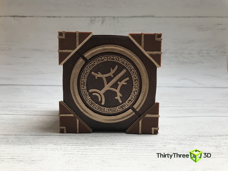 May include: A brown wooden box with a gold-colored circular design on the front. The design features a stylized tree with branches and leaves.