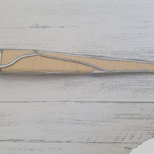 Op de afbeelding: Een houten dolk met een zilverkleurig metalen handvat en een puntige punt. Het handvat heeft een decoratief ontwerp van zilveren lijnen.