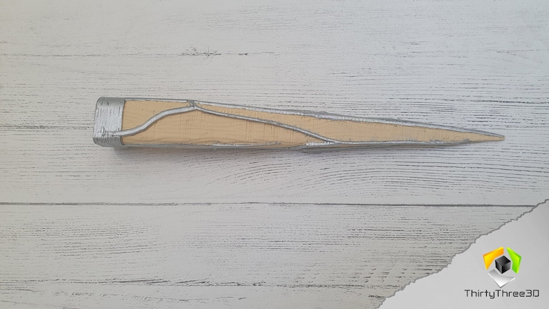 Op de afbeelding: Een houten dolk met een zilverkleurig metalen handvat en een puntige punt. Het handvat heeft een decoratief ontwerp van zilveren lijnen.