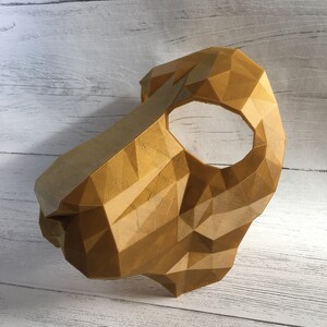 May include: A gold-colored, 3D printed mask with a geometric design. The mask has a single eye hole and is made of a textured material.