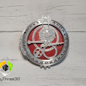 Puede incluir: Una br&uacute;jula de metal de color plateado con un centro rojo y un dise&ntilde;o de lobo. La br&uacute;jula tiene n&uacute;meros alrededor del borde y una serie de engranajes en el centro.