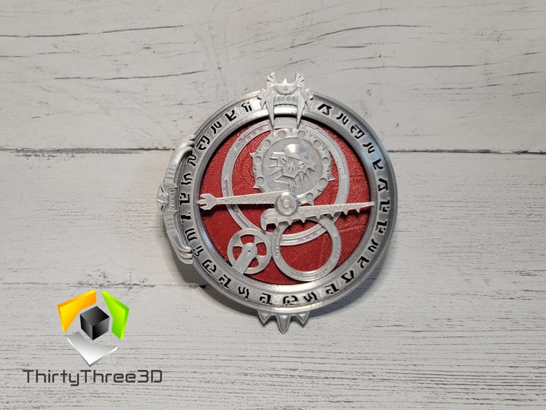 Puede incluir: Una br&uacute;jula de metal de color plateado con un centro rojo y un dise&ntilde;o de lobo. La br&uacute;jula tiene n&uacute;meros alrededor del borde y una serie de engranajes en el centro.