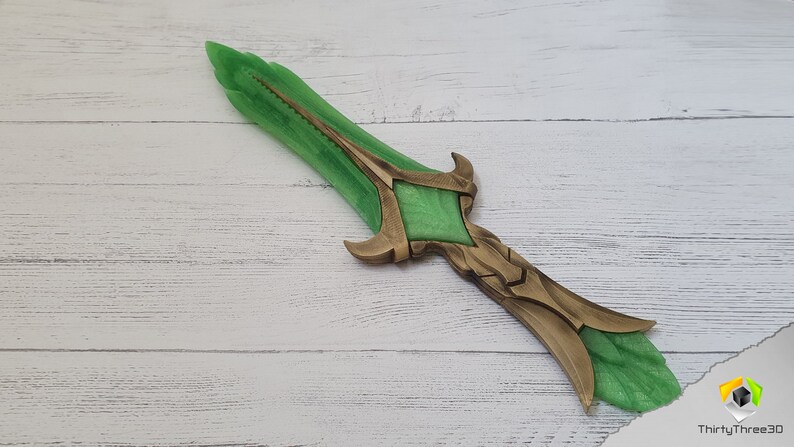 May include: A green and gold fantasy dagger with a detailed design. The blade is green and the hilt is gold with intricate details.