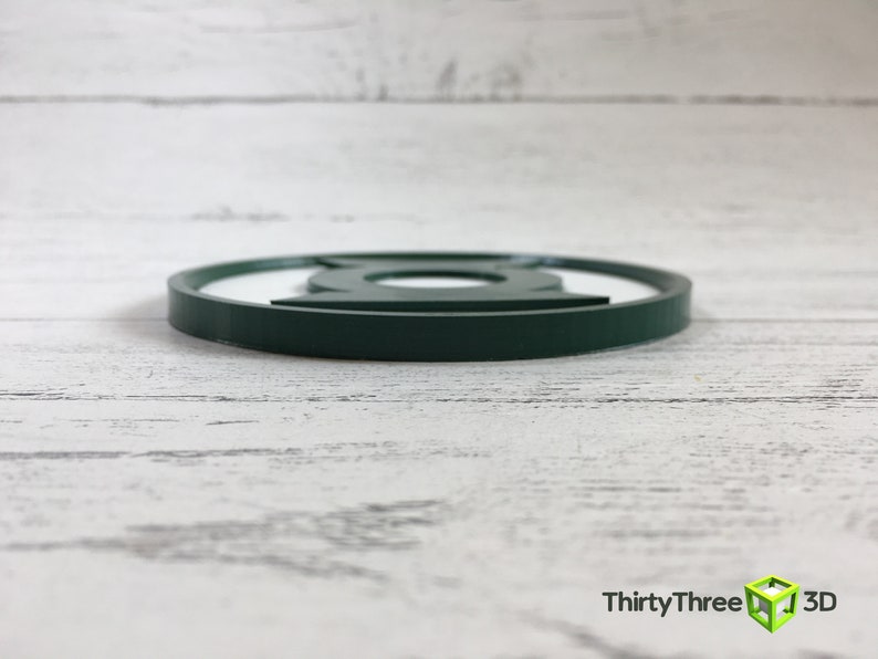 Puede incluir: Posavasos redondo de color verde oscuro con el logotipo de Linterna Verde.