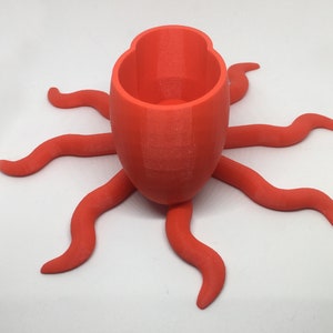 May include: A bright orange 3D printed octopus planter with a round pot on top. The planter has eight tentacles.