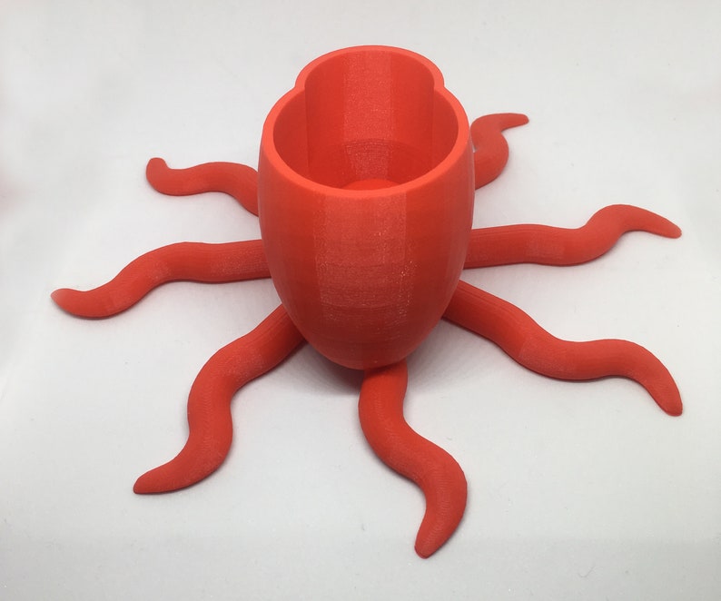 May include: A bright orange 3D printed octopus planter with a round pot on top. The planter has eight tentacles.