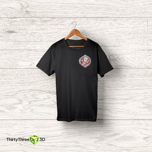 May include: Black t-shirt with a silver and red circular graphic on the left chest. The graphic features a stylized design with a skull and crossbones.