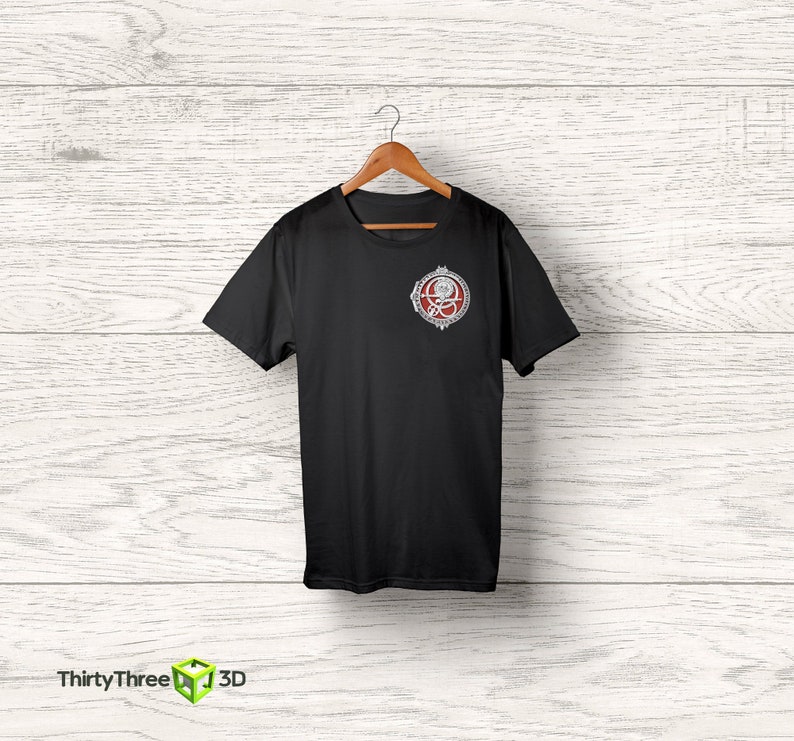 May include: Black t-shirt with a silver and red circular graphic on the left chest. The graphic features a stylized design with a skull and crossbones.