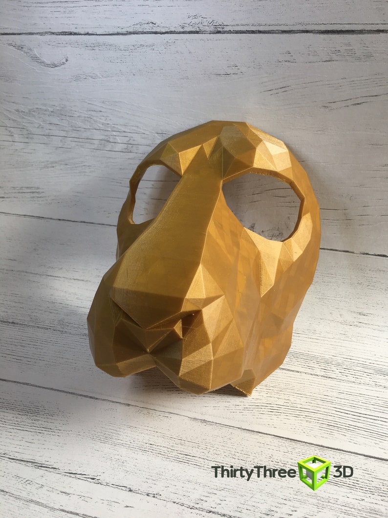 May include: A gold-colored, 3D printed mask with a geometric design. The mask has two eye holes and a prominent nose.