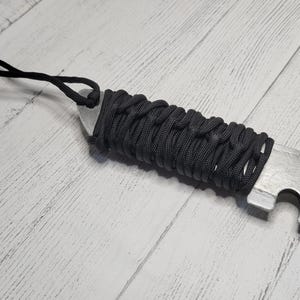 Peut inclure: Un couteau &agrave; lame argent&eacute;e envelopp&eacute; de paracorde noir avec un ouvre-bouteille. Le couteau est dot&eacute; d'un cordon noir attach&eacute; &agrave; la poign&eacute;e.