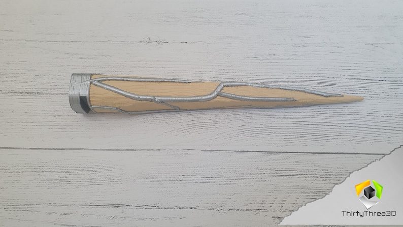 Op de afbeelding: Een beige en zilveren 3D-geprint rekwisietwapen met een puntige punt en een textuur.