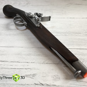 Puede incluir: Una r&eacute;plica de pistola de chispa con culata de madera oscura y componentes met&aacute;licos. La pistola tiene gatillo, martillo y ca&ntilde;&oacute;n. El extremo del ca&ntilde;&oacute;n tiene una punta naranja. La imagen tambi&eacute;n incluye el texto "ThirtyThree 3D".