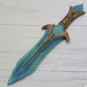 May include: A blue and gold fantasy-style dagger with a detailed design. The blade is translucent and has a frosted finish. The hilt is gold and has intricate carvings.