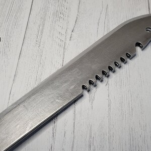 Peut inclure: Un couteau argent&eacute; avec une lame dentel&eacute;e et une pointe pointue. Le couteau est pos&eacute; sur une surface en bois blanc.