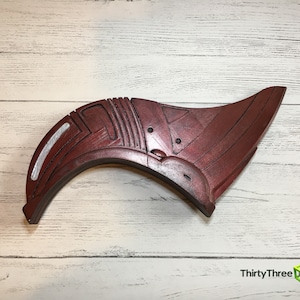 May include: A red and silver 3D printed prop shaped like a curved wing with intricate details. The prop is made of plastic and has a smooth finish.
