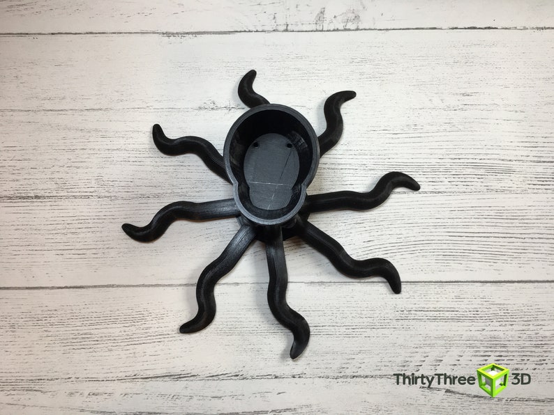 May include: Black octopus-shaped planter with eight tentacles. The planter is made of 3D printed plastic and has a smooth, matte finish.