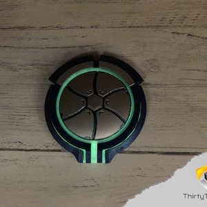 May include: A circular, 3D printed object with a black and green design. The object has a central, silver-colored, star-shaped design.