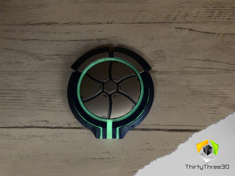 May include: A circular, 3D printed object with a black and green design. The object has a central, silver-colored, star-shaped design.