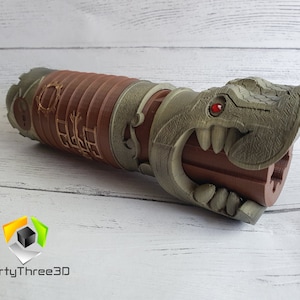 May include: A 3D printed lightsaber hilt with a dragon head design. The hilt is brown and has a red gem for an eye. The dragon's mouth is open and has sharp teeth.