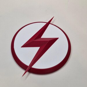 May include: A red lightning bolt emblem on a white circle with a red border. The emblem is a stylized lightning bolt, with sharp angles and a three-dimensional appearance. The design is set against a plain white background.